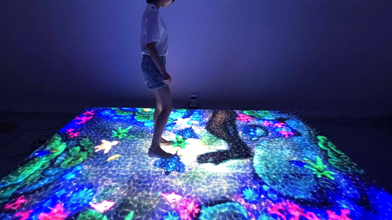 Visitor standing on an interactive LED floor showing an underwater scene